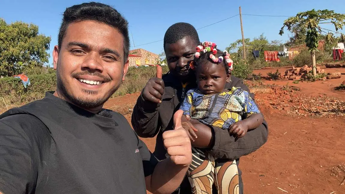 Saif taking a selfie with a man holding his baby on a red dirt road